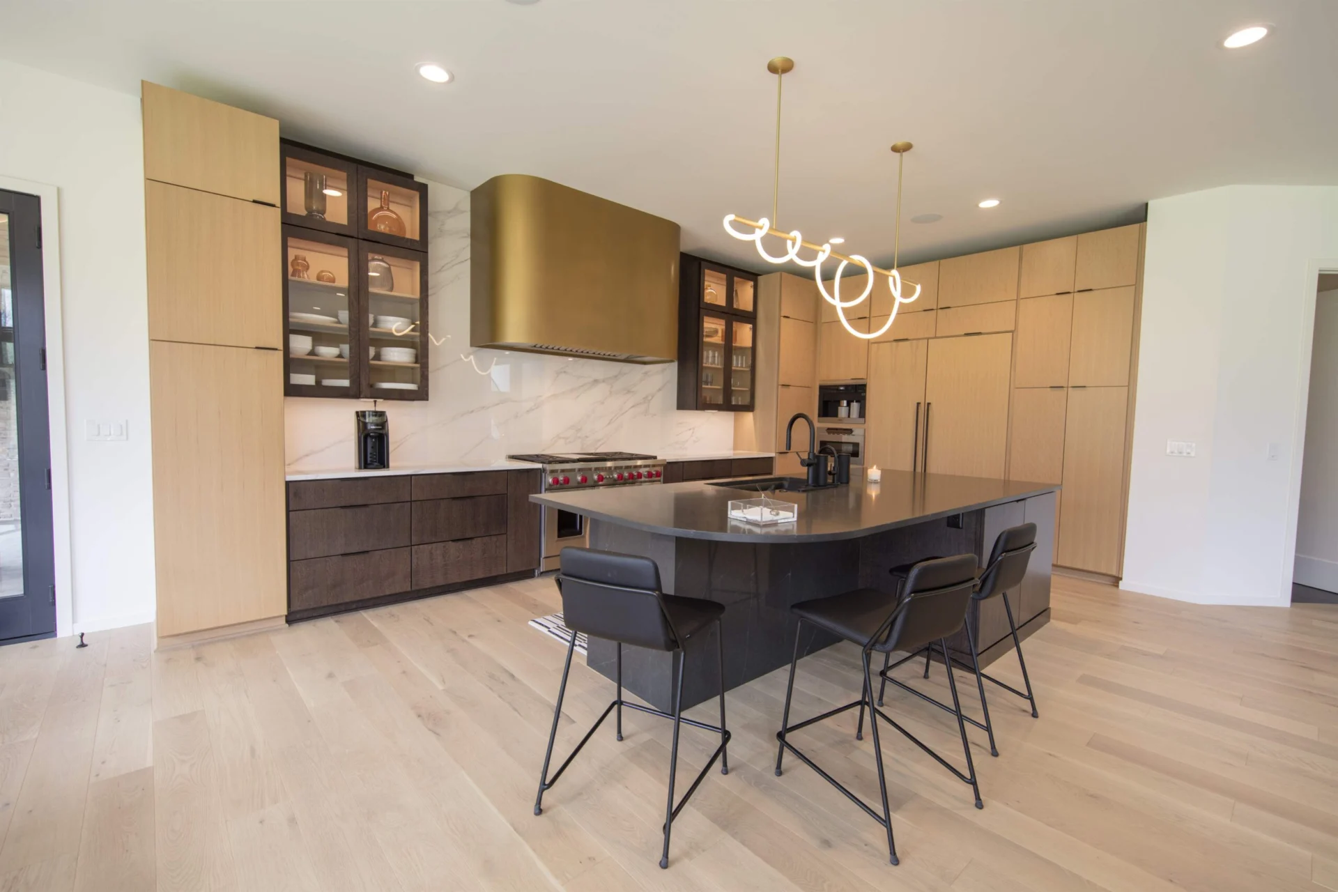 Contemporary kitchen in quarter sawn white oak with a black waterfall island and brass hood