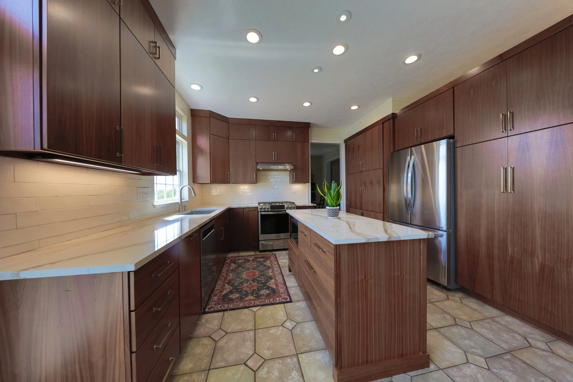 Rich walnut slab-front kitchen cabinetry with veined quartzite counters and brass pulls