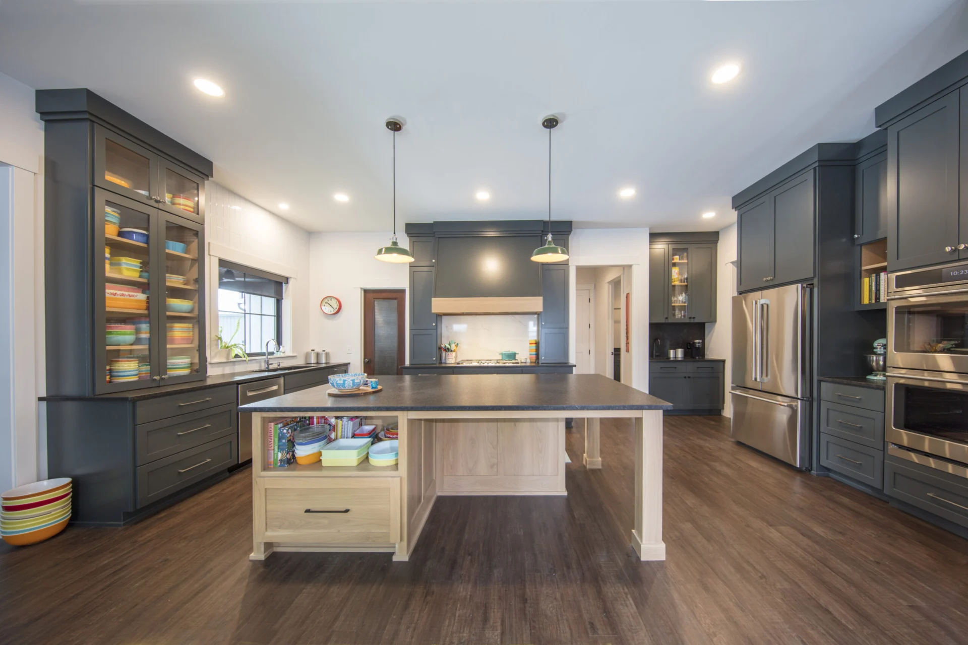 Deep slate painted kitchen cabinetry with a natural white oak island and dark stone counters